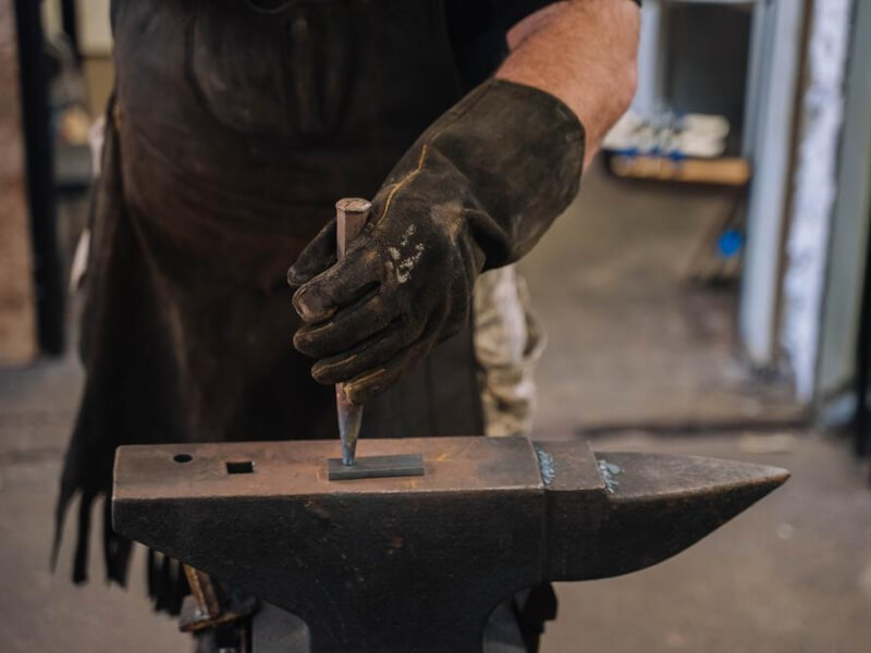 Close up of a hammer striking a piece of metal on a blacksmith's anvil